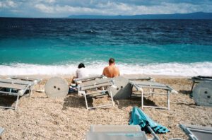 couple sitting on a beach in croatia overlooking the mountains across a turquoise sea