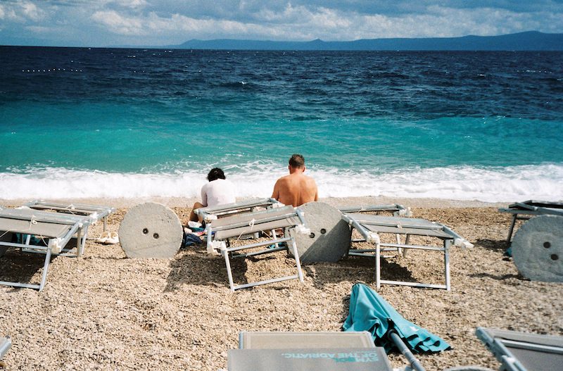 couple sitting on a beach in croatia overlooking the mountains across a turquoise sea
